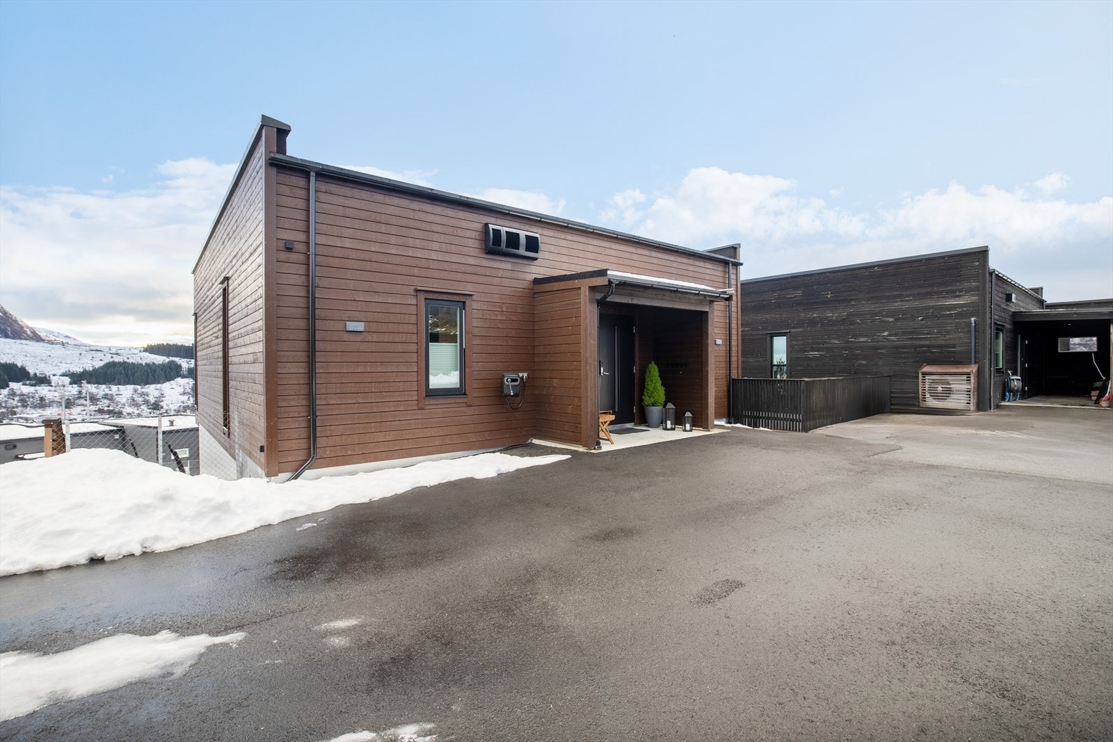 Fasade mot nord med stort asfaltert parkeringsområde, garasje og hovedinngang. Galleribilde