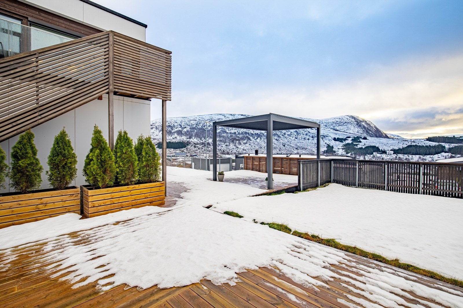 Sørvendt uteområde med hage, stor markterrasse, pergola og trapp til altan og hovedinngang. Galleribilde