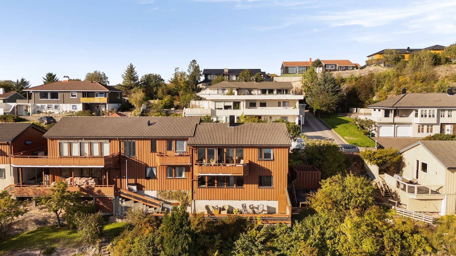Bygningen er en vertikaldelt tomannsbolig med moderne trekledning og flere utkragede balkonger. Galleribilde