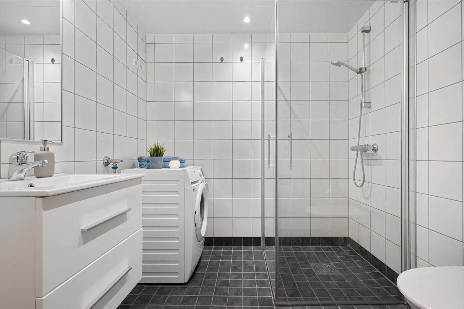 Flislagte vegger og gulv med dusjhjørne og opplegg for vaskemaskin gir et funksjonelt bad. Galleribilde