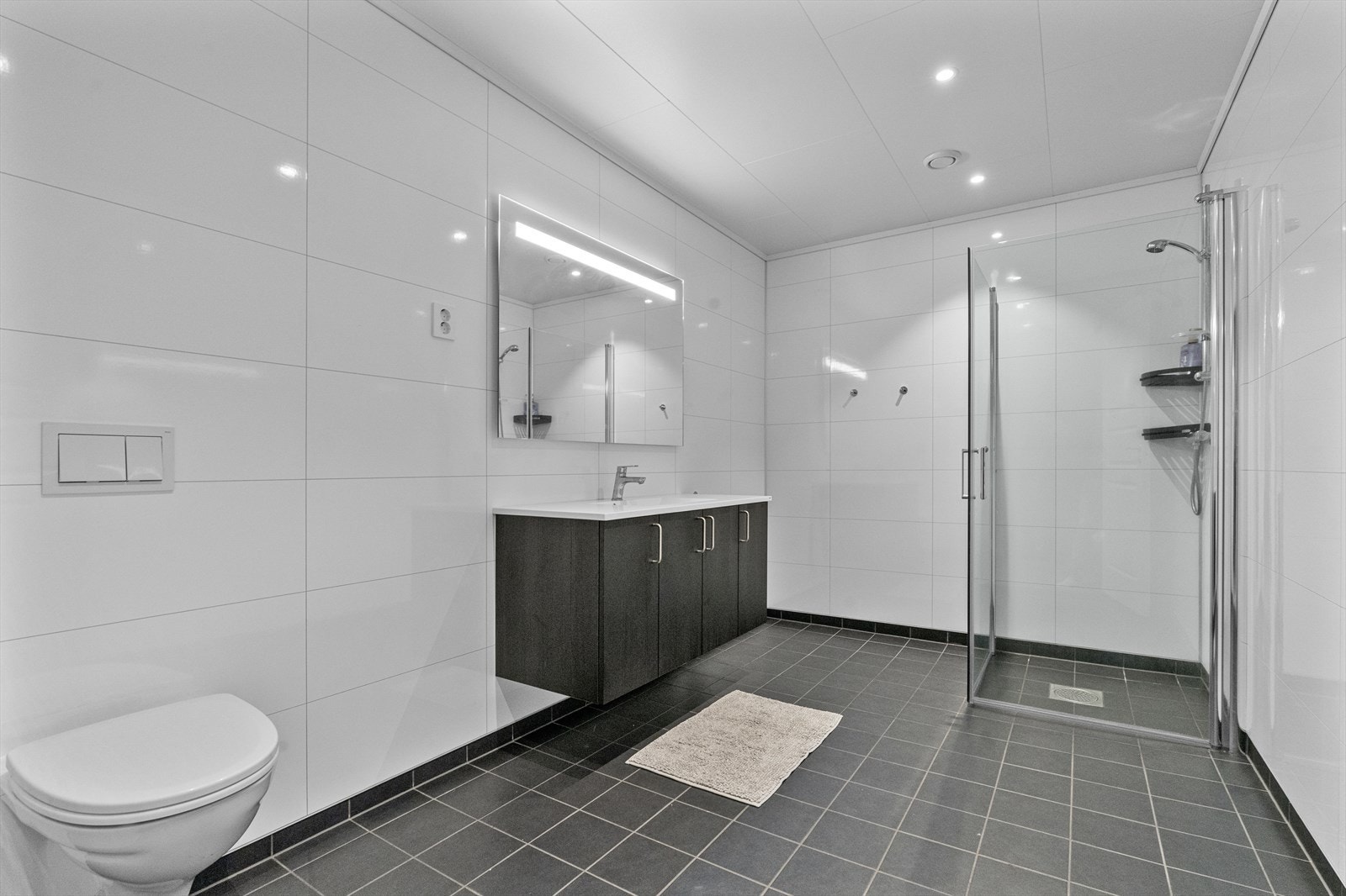 Badet har tidløse overflater, flislagt golv med varmekablar og downlights i himling Galleribilde