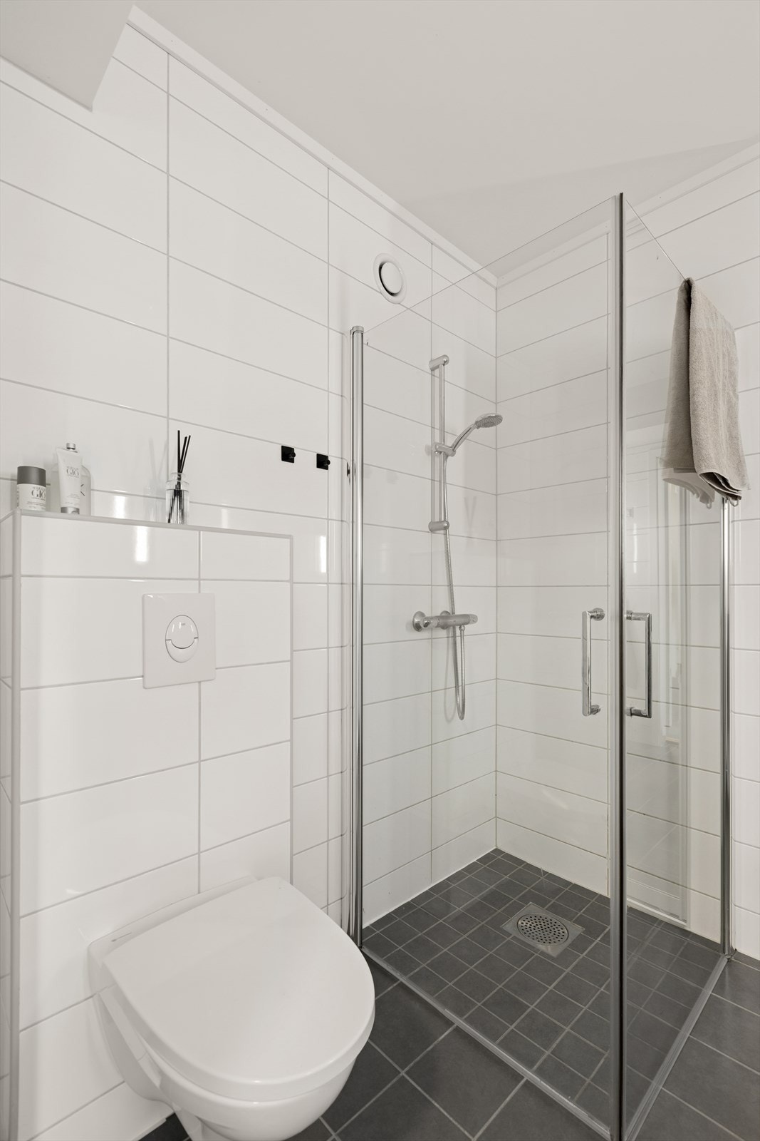 Badet utstyrt med dusjhjørne med glassdører, vegghengt toalett, servantinnredning, varmtvannsbereder og opplegg for vaskemaskin. Galleribilde