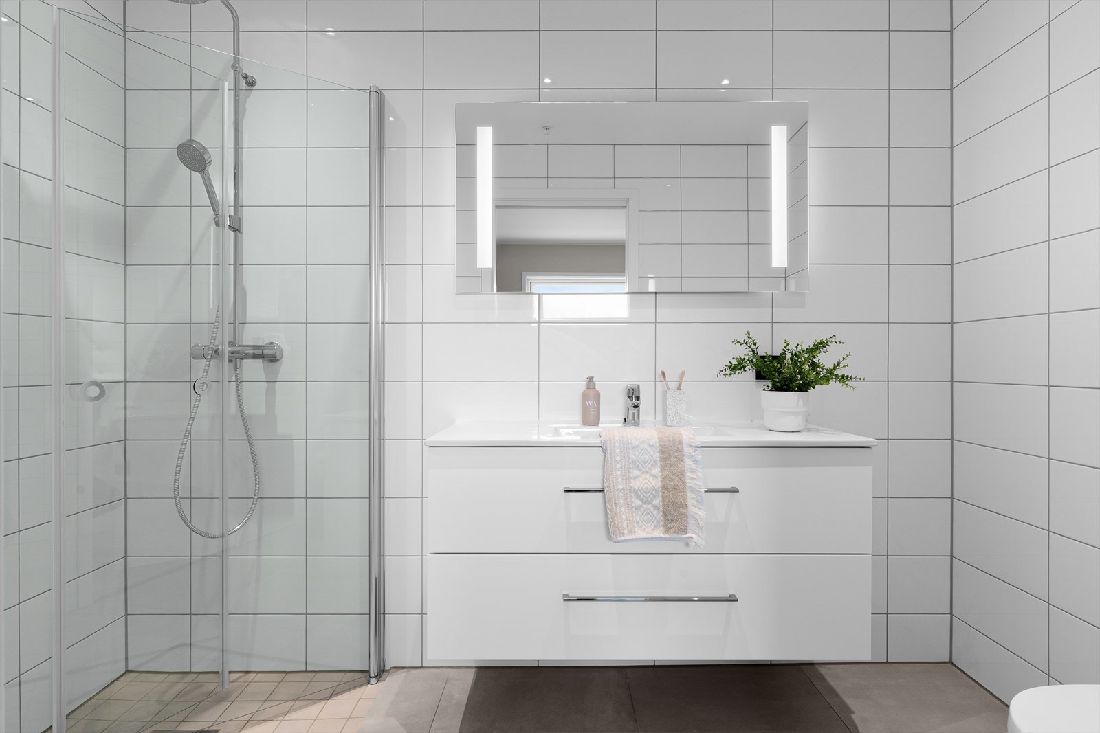 Pent helfliset bad som inneholder vegghengt wc, dusjhjørne og baderomsinnredning i hvit utførelse. (Bilde tatt fra H0401) Galleribilde