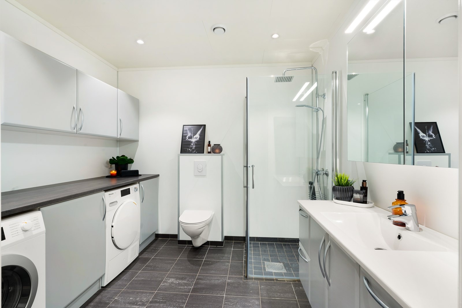 Det er utstyrt med vegghengt toalett, dusjhjørne med glassvegger og hvit baderomsinnredning med heldekkende servant, speilskap og belysning. Galleribilde