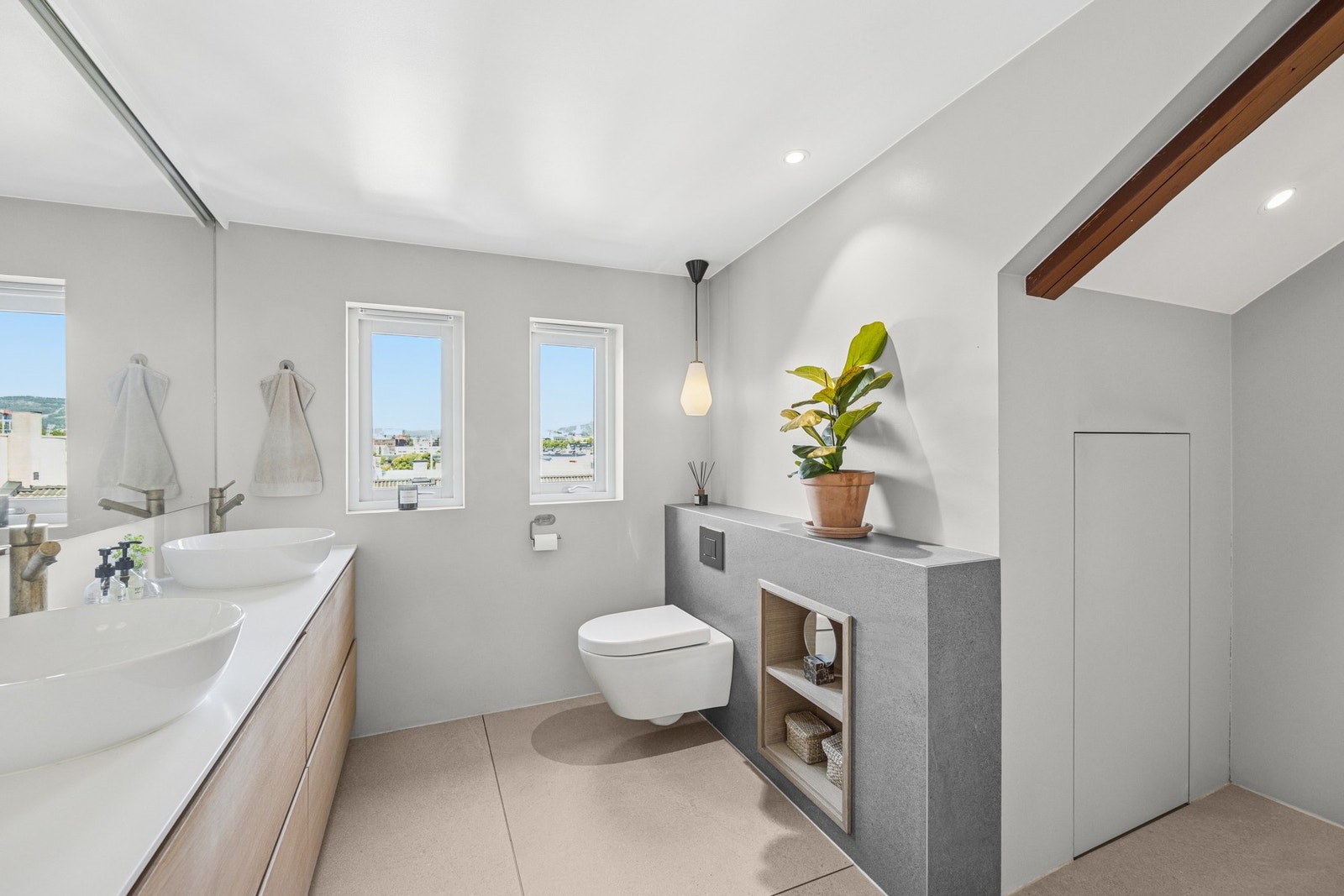 Lekkert flislagt bad med veggmontert toalett, dusjhjørne, dobbel servant, skap, speil og belysning. Galleribilde