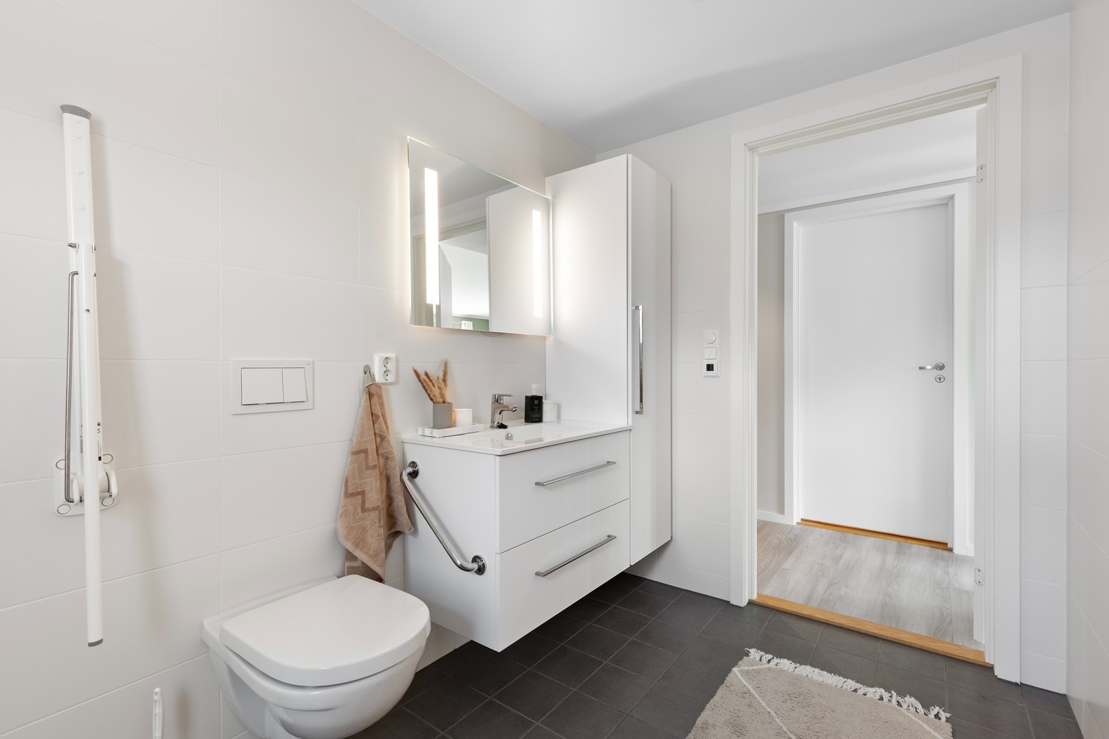 Badet har gulvflis, veggflis og lysmalt himling med downlights. Bad er utstyrt med veggtoalett, vask over innredning og dusjnisje.. Galleribilde