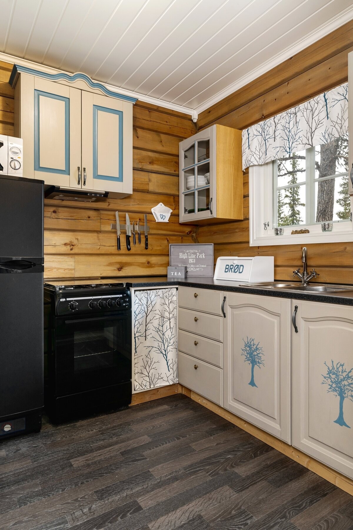 Kjøkkeninnredning i laminat/finerte plater med under- og overskap med malte profilerte dører/fronter. Komfyr og kjøleskap. Kjøkkenet har samme vannsystem som i hytta. Galleribilde