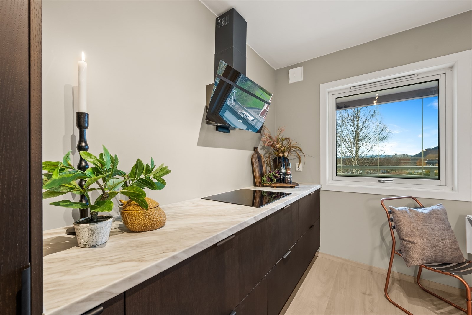 Kjøkkenet byr på en praktisk utforming og strekker seg fra vegg til vegg, noe som bidrar til mye benkeplass. Det er vegghengt kjøkkenventilator med kullfilter. Galleribilde