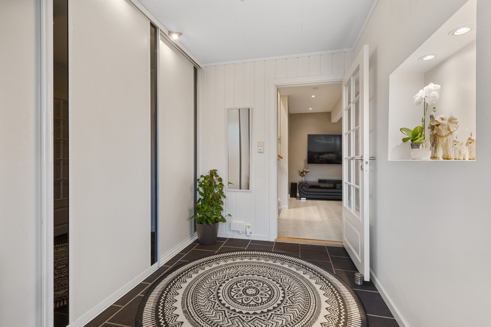 En lys og innbydende, flislagt entré med behagelig gulvvarme som gir ekstra komfort. Entreen fremstår både praktisk og stilren, og er utstyrt med en romslig skyvedørsgarderobe som byr på rikelig med oppbevaringsplass. Galleribilde