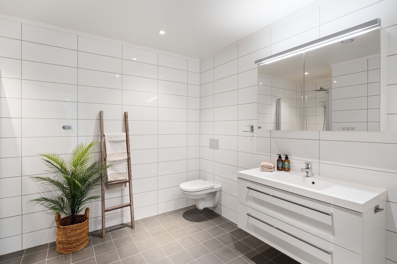 Bad 1 med flislagte overflater, servantinnredning, vegghengt toalett og dusjvegger i glass. Galleribilde