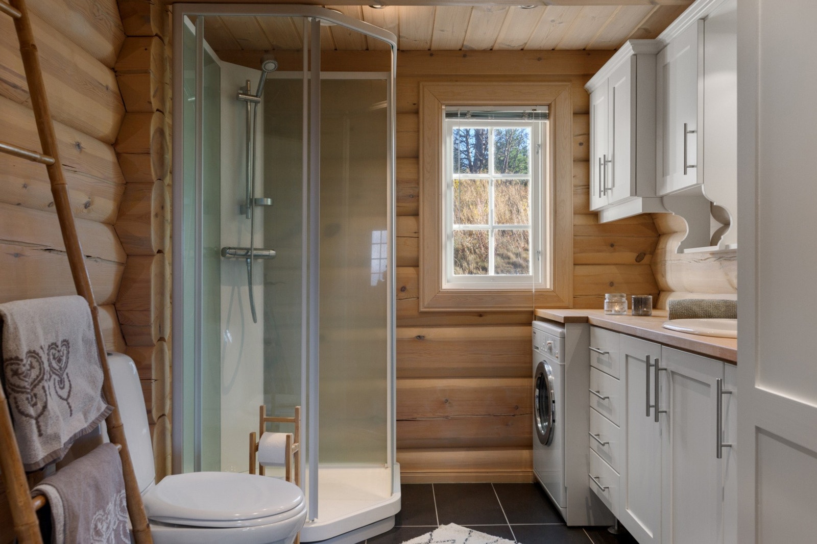 Lunt og fint bad med vegger i tømmer, og flislagt gulv med varmekabler. Bad har montert klosett, servant, dusjkabinett og opplegg til vaskemaskin. Galleribilde