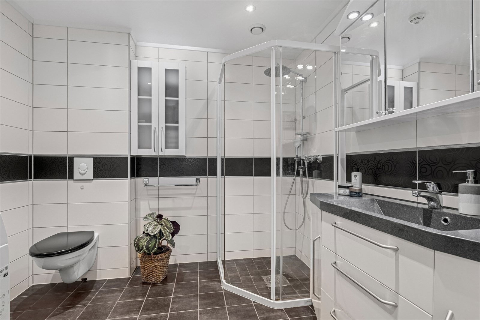 Delikat helfliset bad med varme i gulv. Rommet har innredning med innfelt forkant vask, veggmontert toalett, dusjvegger/hjørne og opplegg for vaskemaskin. Ventil i himling tilknyttet balansert ventilasjon. Galleribilde