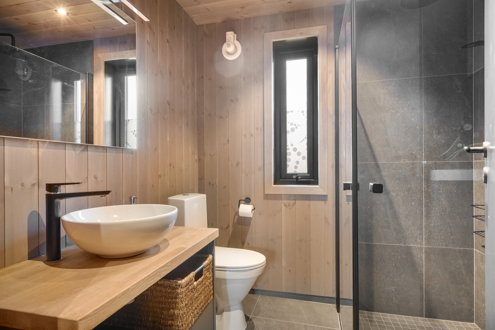 Badet har fliser med varme på gulv, fliser i dusjsone, og ellers panelte overflater. Servantinnredning, toalett og dusjvegger i glass. Galleribilde