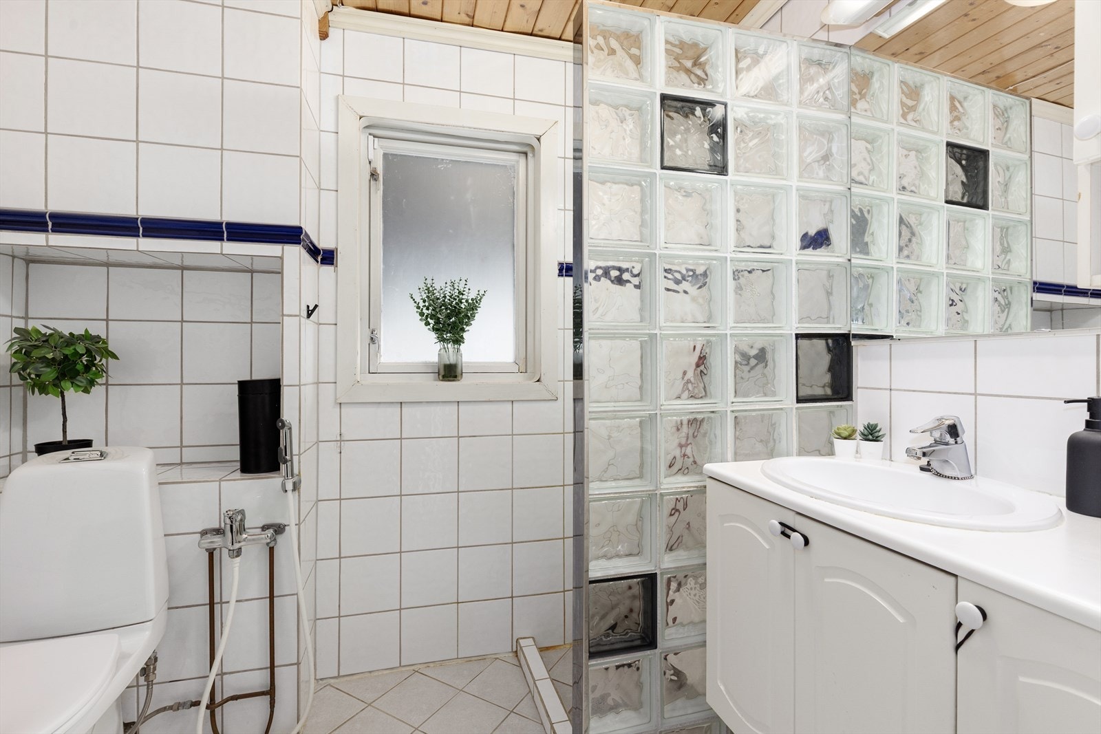 Lyst, flislagt bad fra 2005. Her er det varmekabler i gulv, toalett og hånddusj på vegg, samt dusjnisje og servantinnredning. Galleribilde