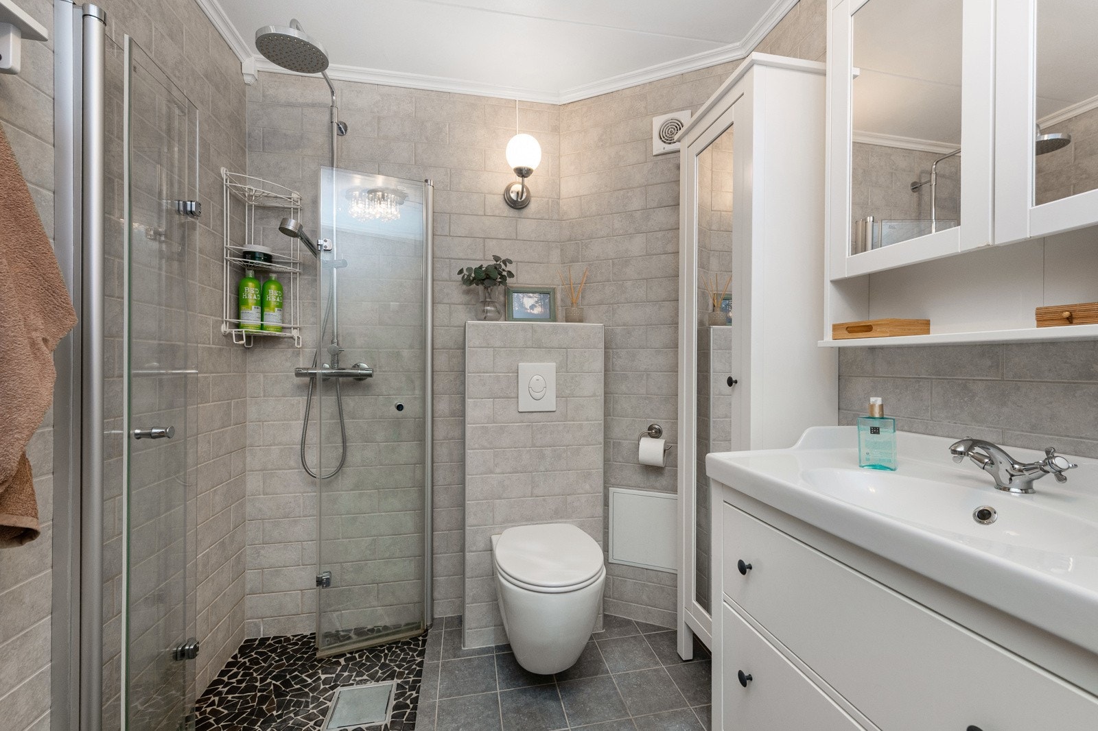 Dusjhjørne med glassvegger. Hvit baderomsinnredning med heldekkende vask. Sideskap med speil Galleribilde