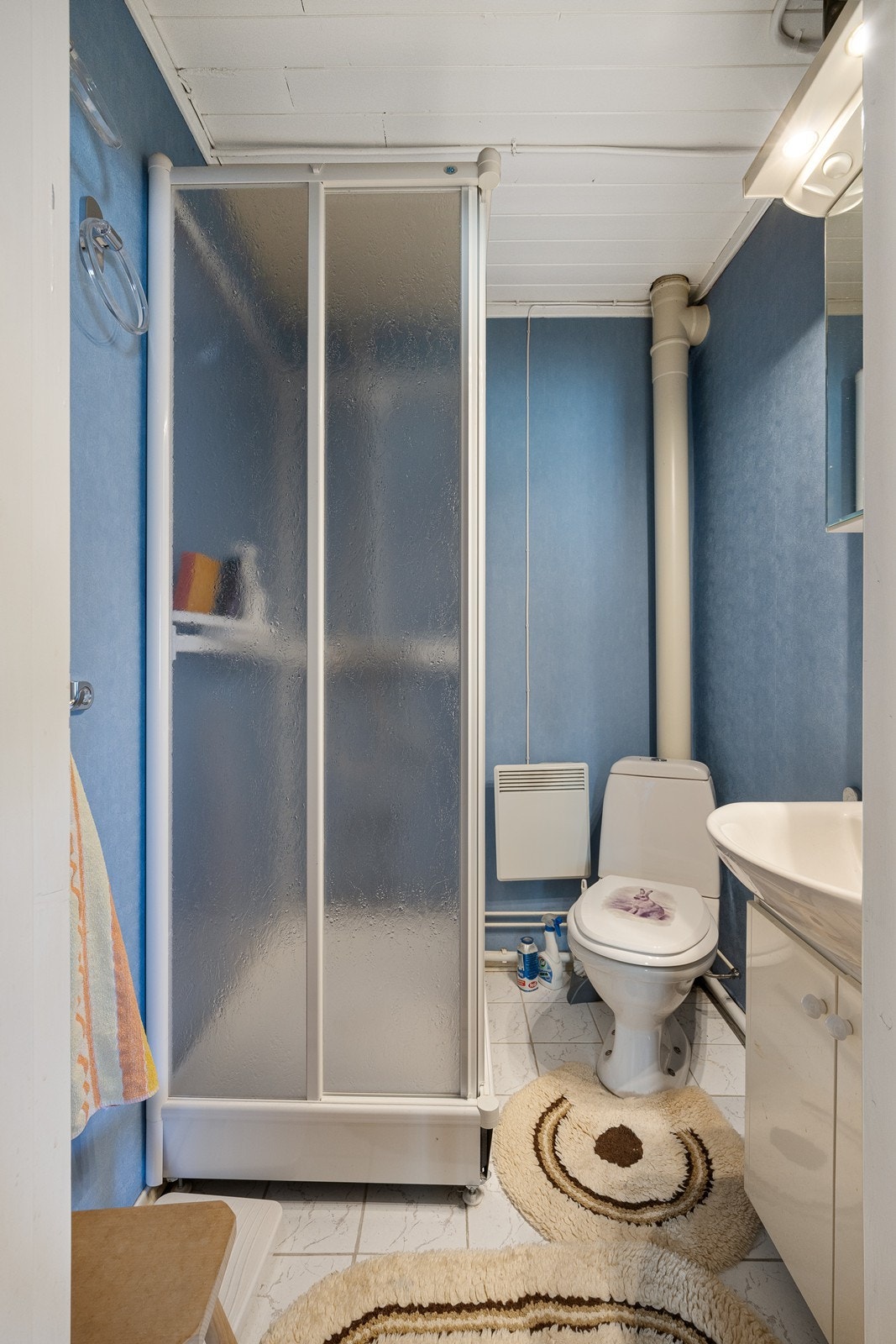 Badet nede har panelovn, gulvfliser og blå tapet på veggene. Vaskerommet ligger vegg i vegg med badet. Galleribilde