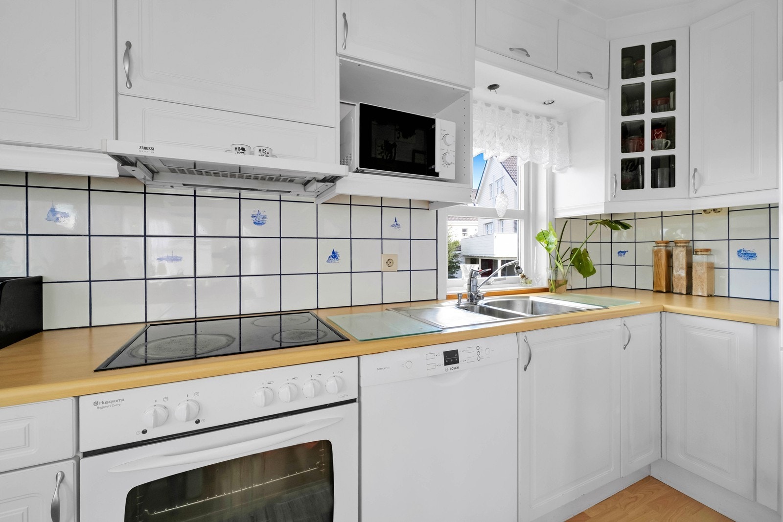 Kjøkkeninnredning med hvite, profilerte fronter og integrert steketopp og komfyr. Opplegg til oppvaskmaskin. Galleribilde