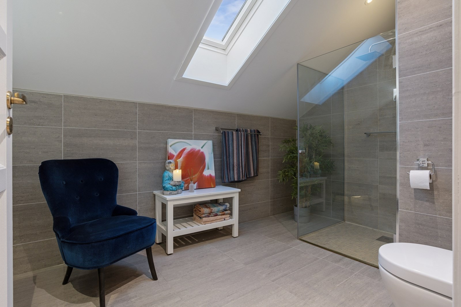 Badet i 2.etg. har keramiske fliser på gulv og vegger og elektriske varmekabler i gulvet. Innredningen består av et vegghengt toalett, dusj med foldedører i glass, samt dobbel servant med møblement, speil og belysning. Galleribilde