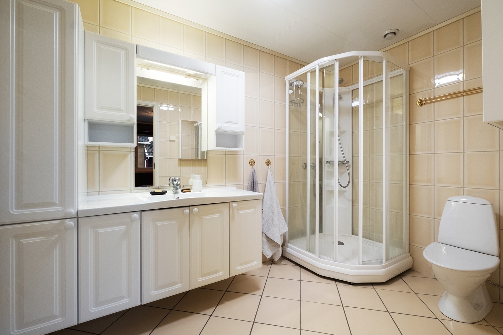 Flislagt bad med varmekabler, utstyrt med dusjkabinett, gulvmontert og innholdsrik baderomsinnredning med hvite, profilerte fronter. Galleribilde