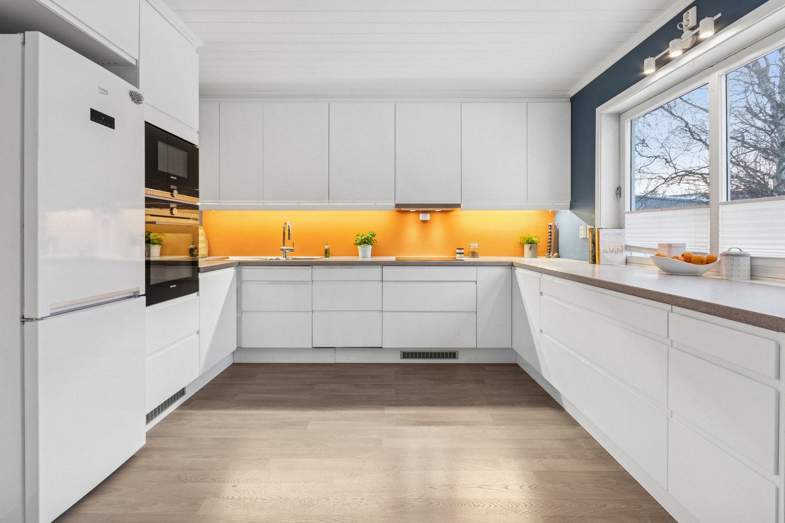 Stilrent kjøkken med glatte fronter, laminat benkeplate og integrerte hvitevarer bestående av kjøl/frys, oppvaskmaskin, komfyr og mikrobølgeovn. Galleribilde