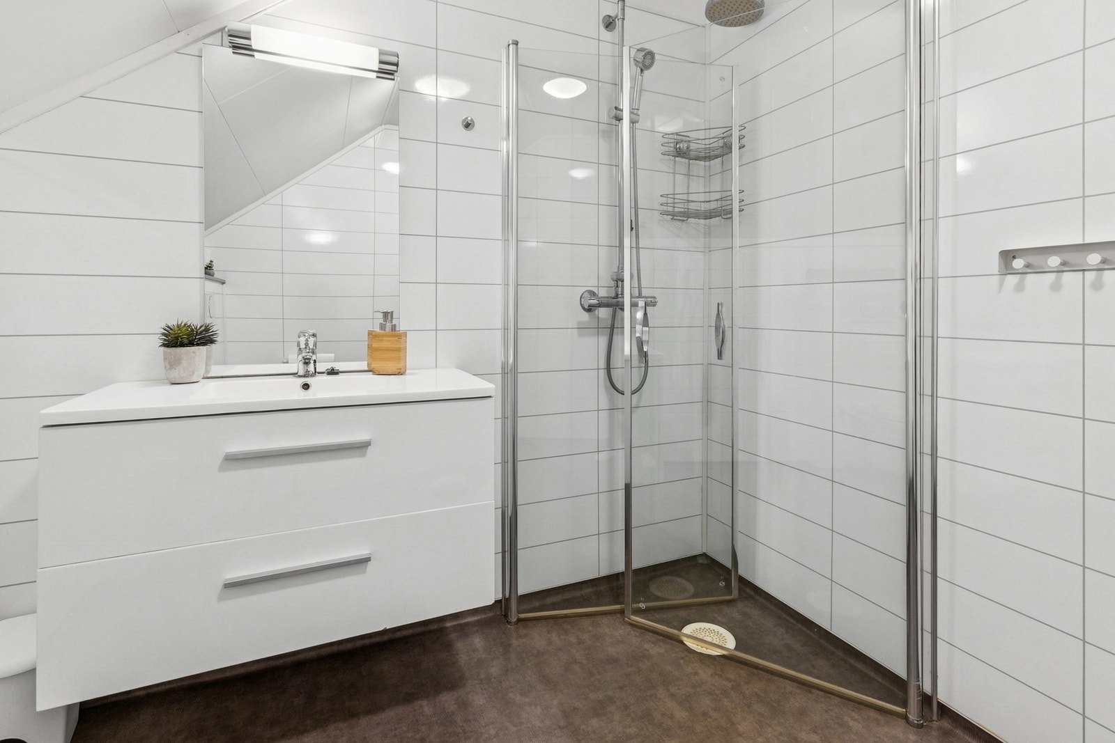 Badet er innredet med nedfelt servant, veggmontert toalett og dusjhjørne. Galleribilde