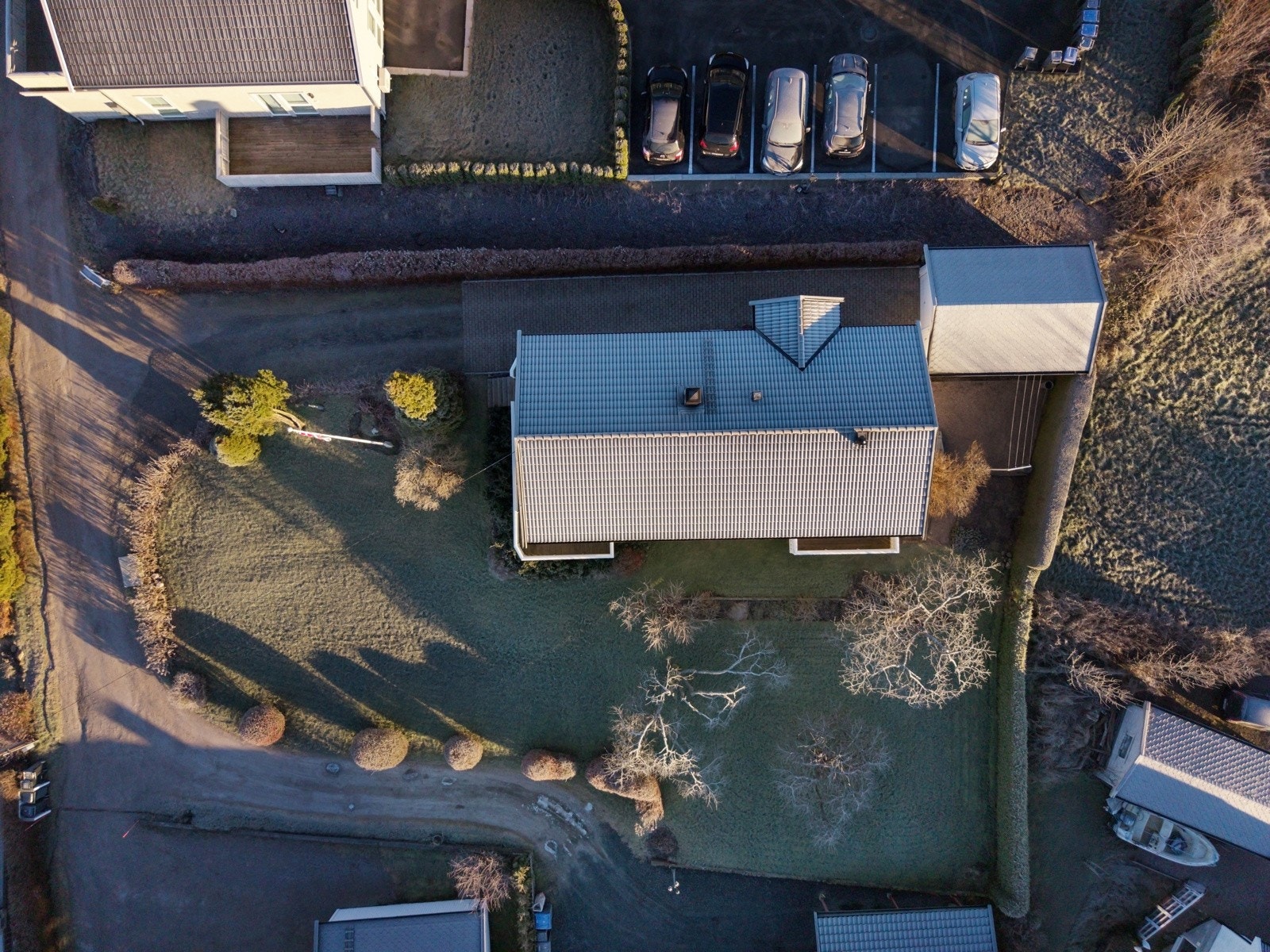 Dronefoto som viser hagen rundt huset. Hekkbeplantning. Flaggstang, Garasje og innglasset vinterhage. Galleribilde