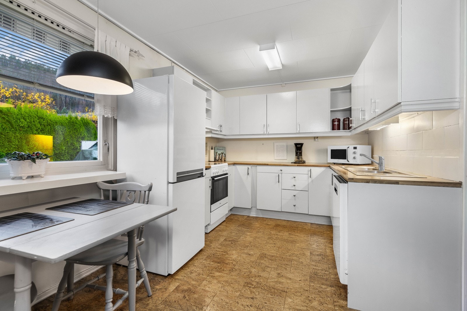 Innredningen består av glatte, hvite fronter og en foliert benkeplate med nedfelt dobbel kum i rustfritt stål. Galleribilde