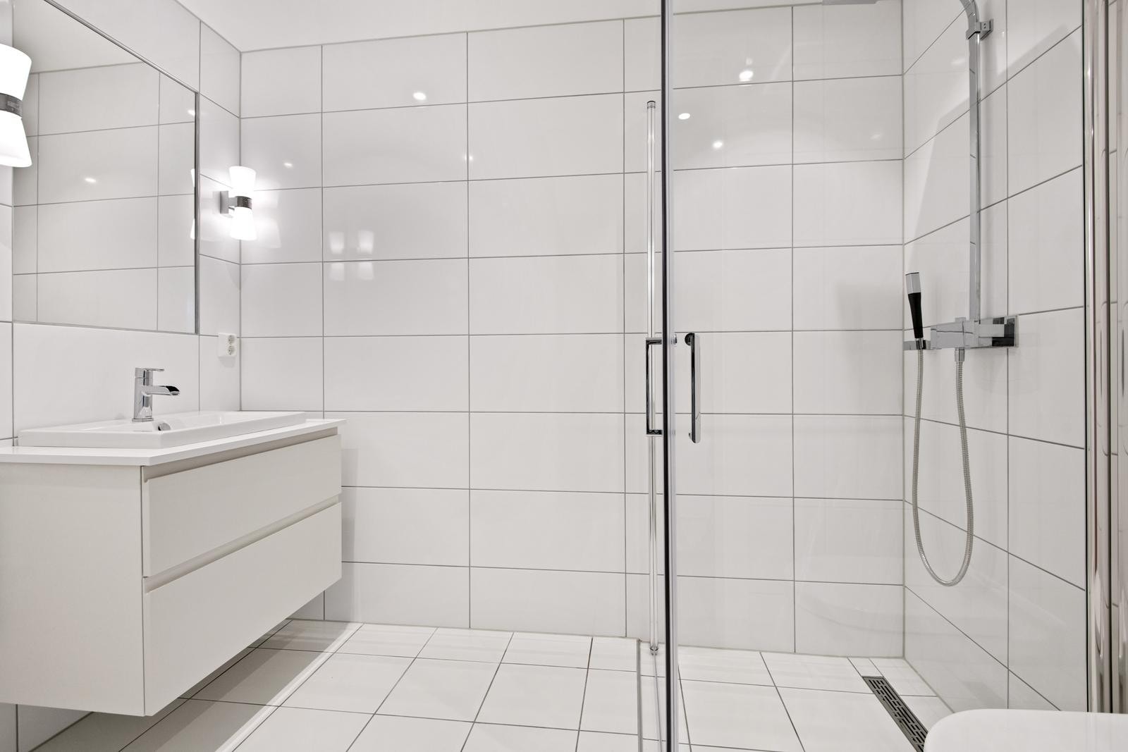 Delikat flislagt bad med gulvvarme, dusj, toalett, servant med underskap og opplegg for vask+tørk Galleribilde