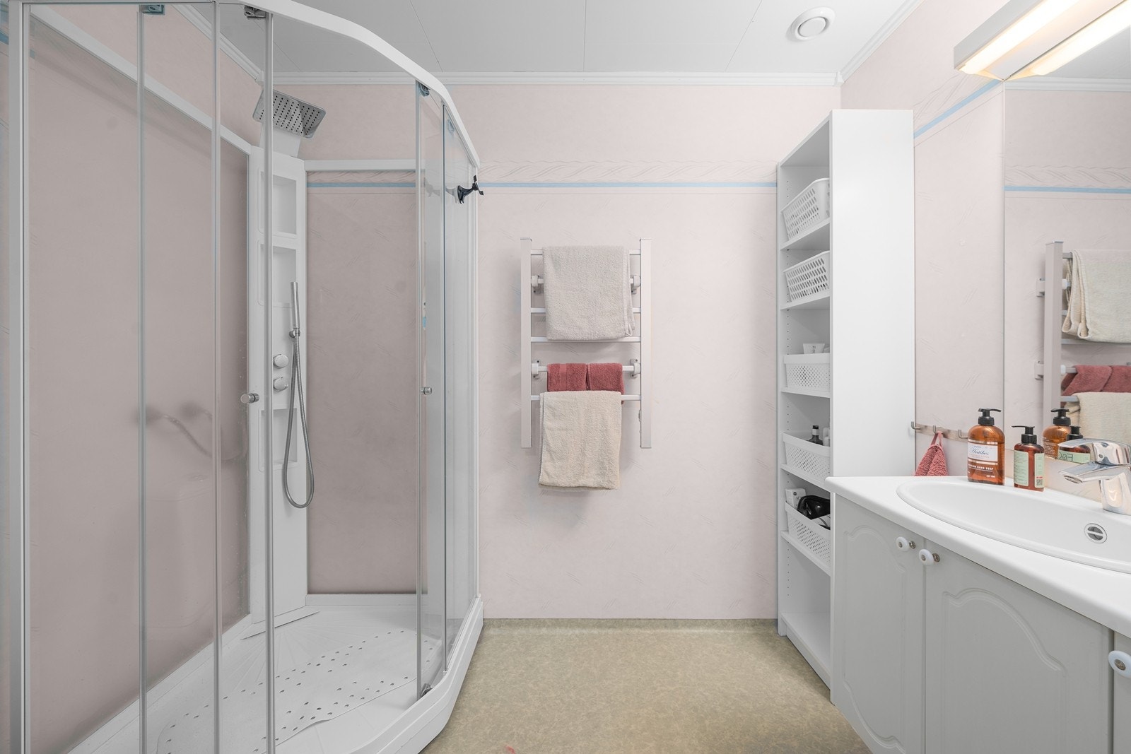 Badet har belegg på gulv og baderomstapet på vegger. Innredningen består av et over og underskap, servant, speil og armatur med stikk og et dusjkabinett. Avtrekk er montert og varmekabler i gulv. Galleribilde