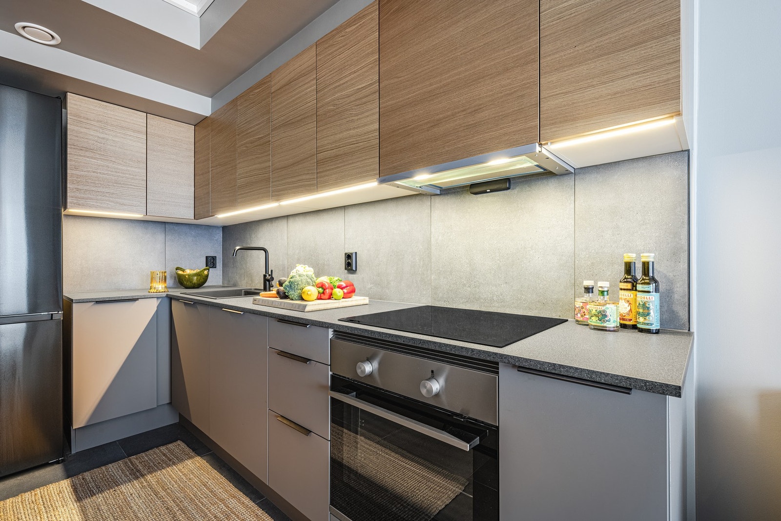 Kjøkken i tidsriktig gråtone med fliser over benk og brytning med eik overskap. Galleribilde