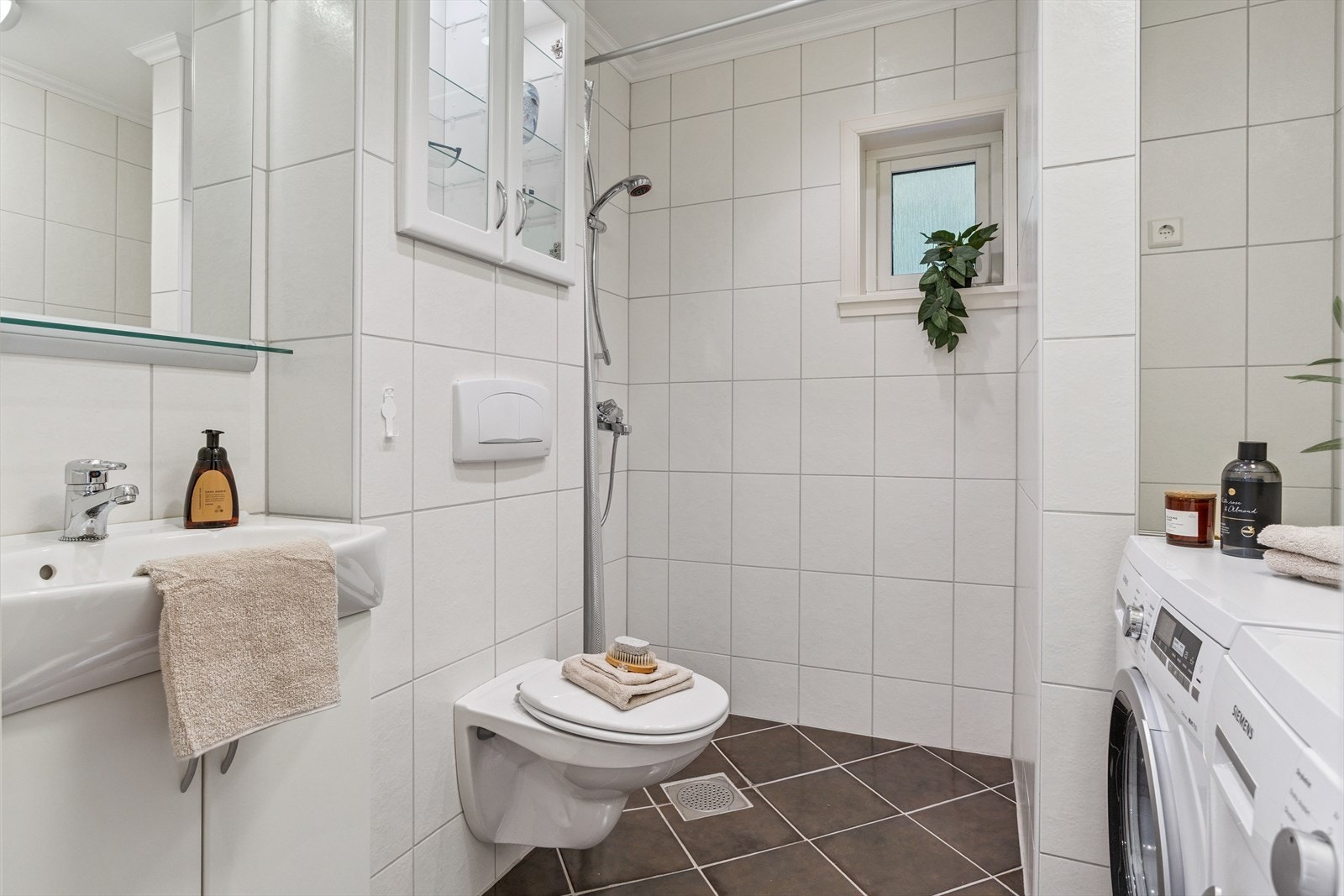 Det andre badet inneholder håndvask med underskap, vegghengt toalett, dusj med forheng og ellers plass til vaskemaskin og tørketrommel. Det er fliser på vegger og gulv, samt varme i gulvet. Galleribilde