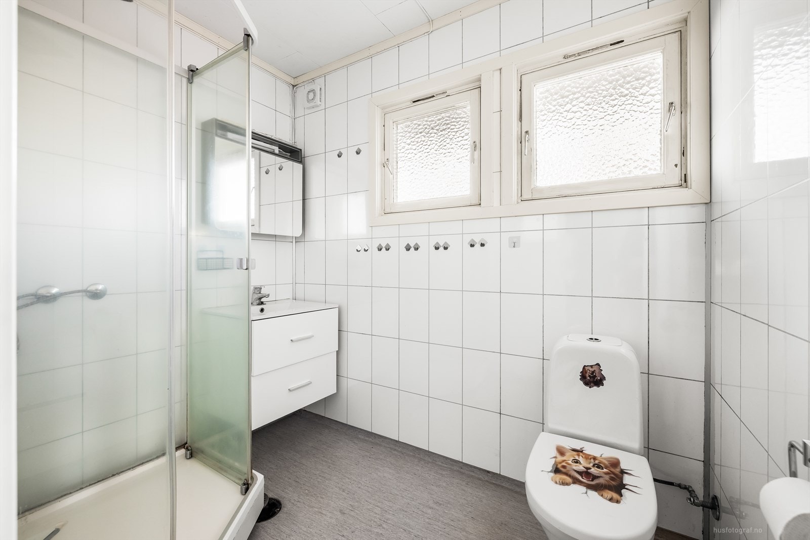 Pent eldre bad med hvit baderoms innredning, speil, dusjkabinett og toalett. Galleribilde