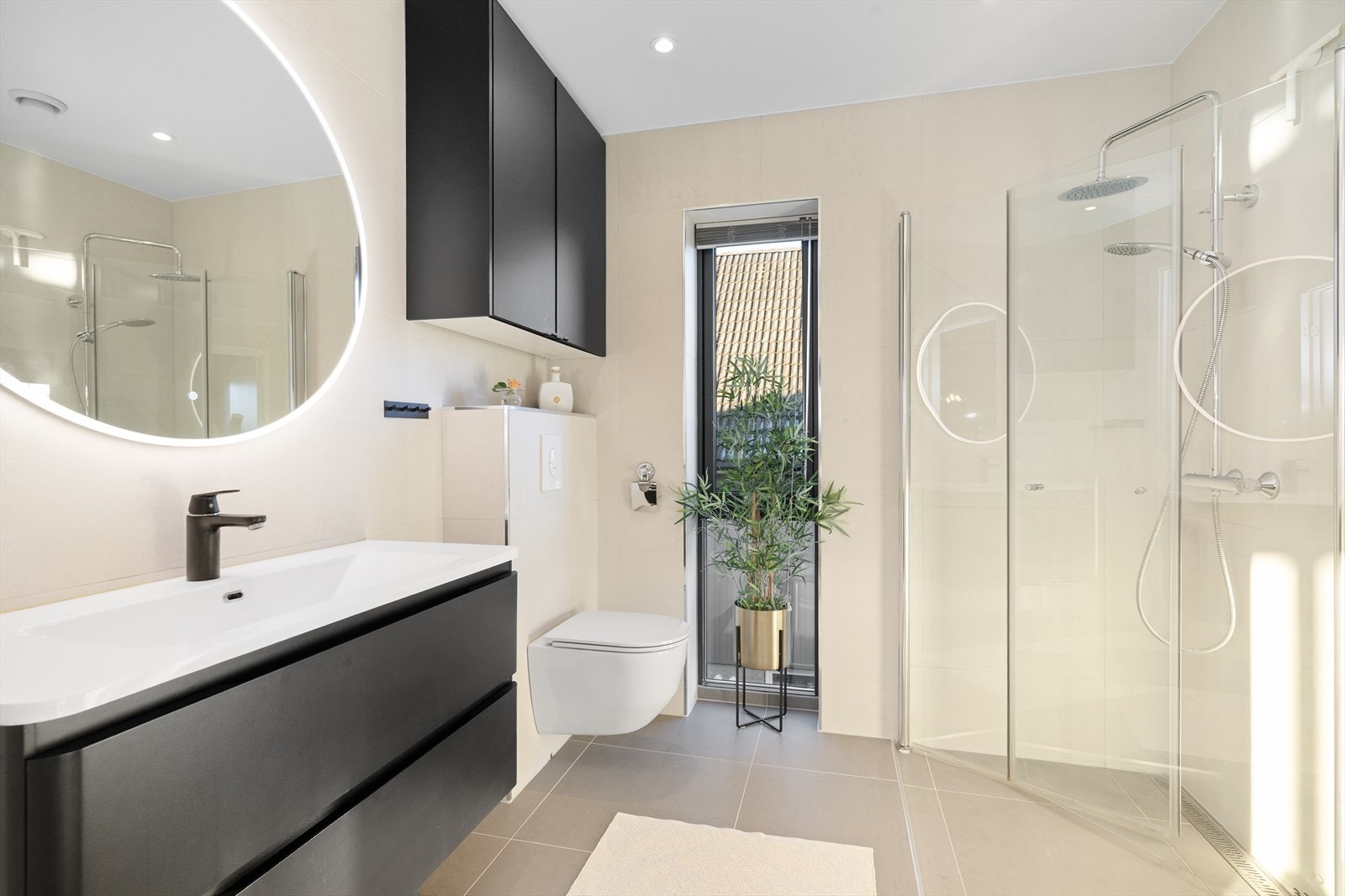 Delikat og moderne baderom som inneholder heldekkende servant med underskap, speil med lys, hjørneskap, vegghengt toalett og dusjhjørne. Galleribilde