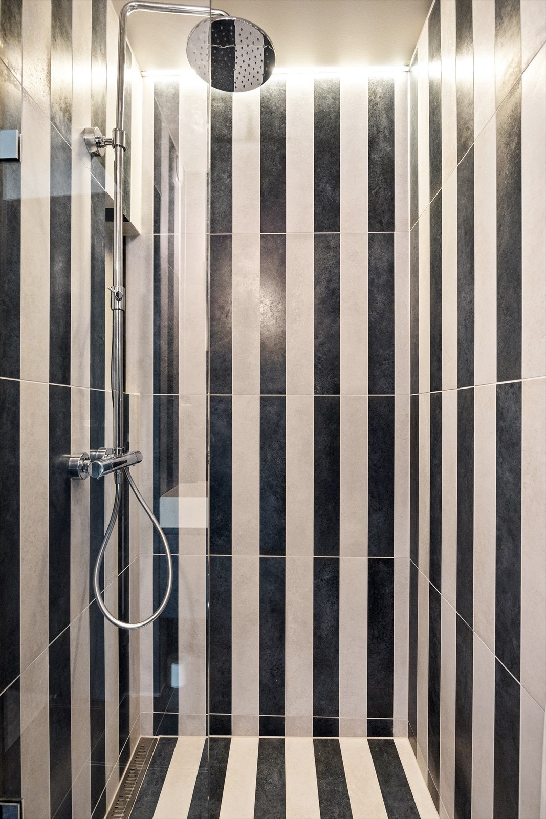 Badet er kledd med stilige italienske fliser av typene "Vulcanica Raku Blu" og "Vulcanica Raku Bianco," som gir rommet et elegant og moderne uttrykk. Galleribilde