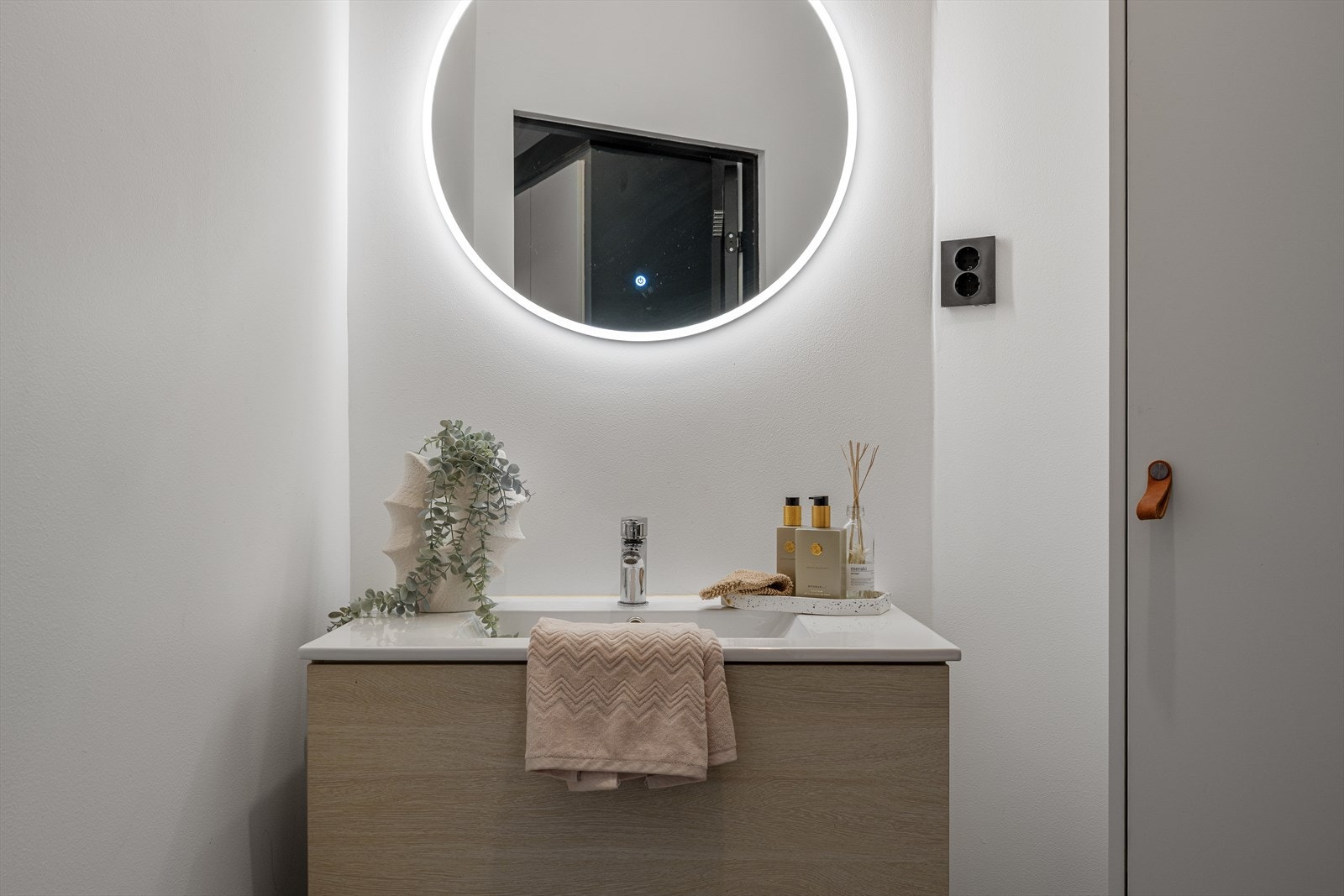 Moderne baderomsinnredning med servant, oppbevaring og rundt speil med integrert belysning Galleribilde