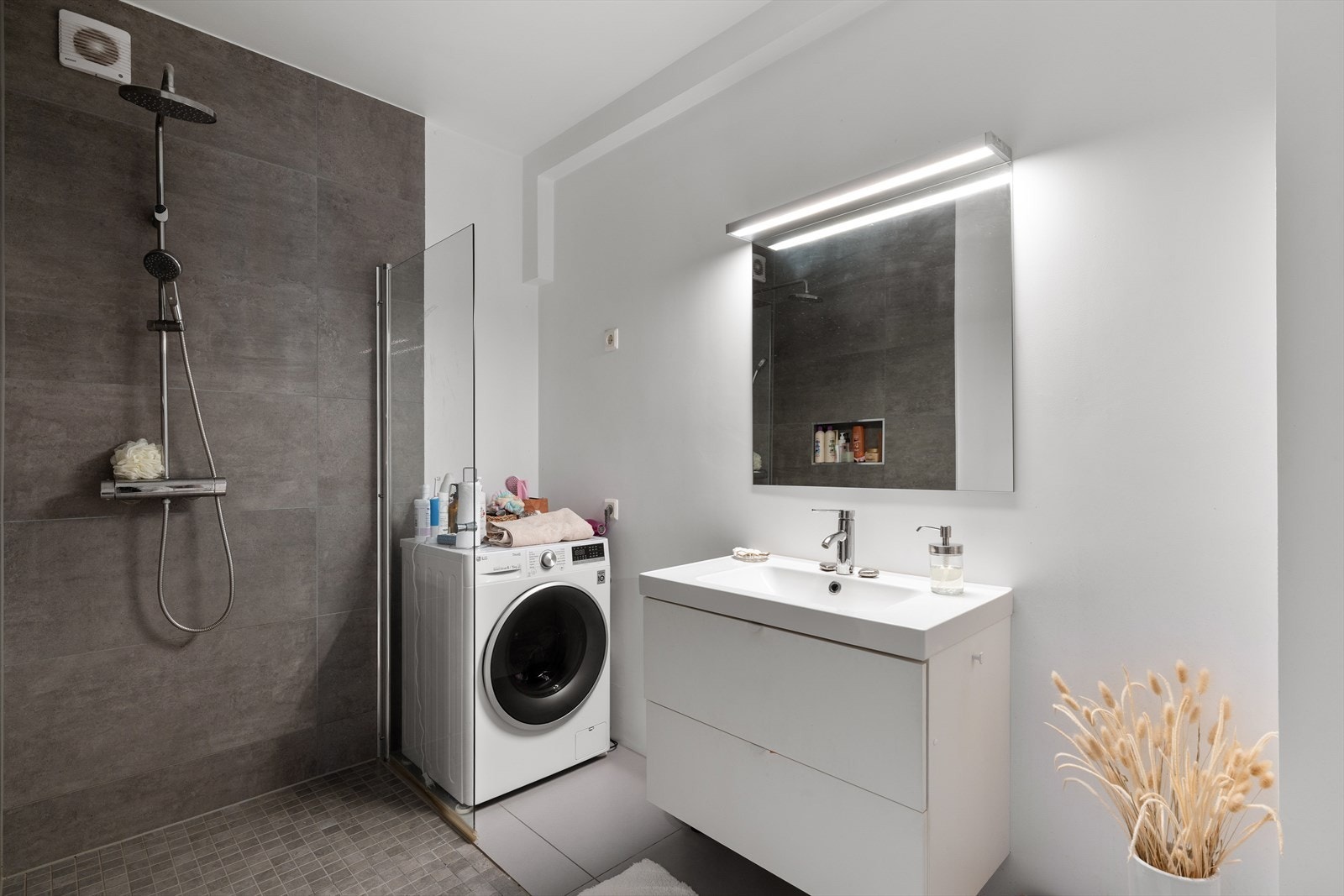 Flislagt bad med dusjhjørne, servant med underskap og opplegg for vaskemaskin. Galleribilde