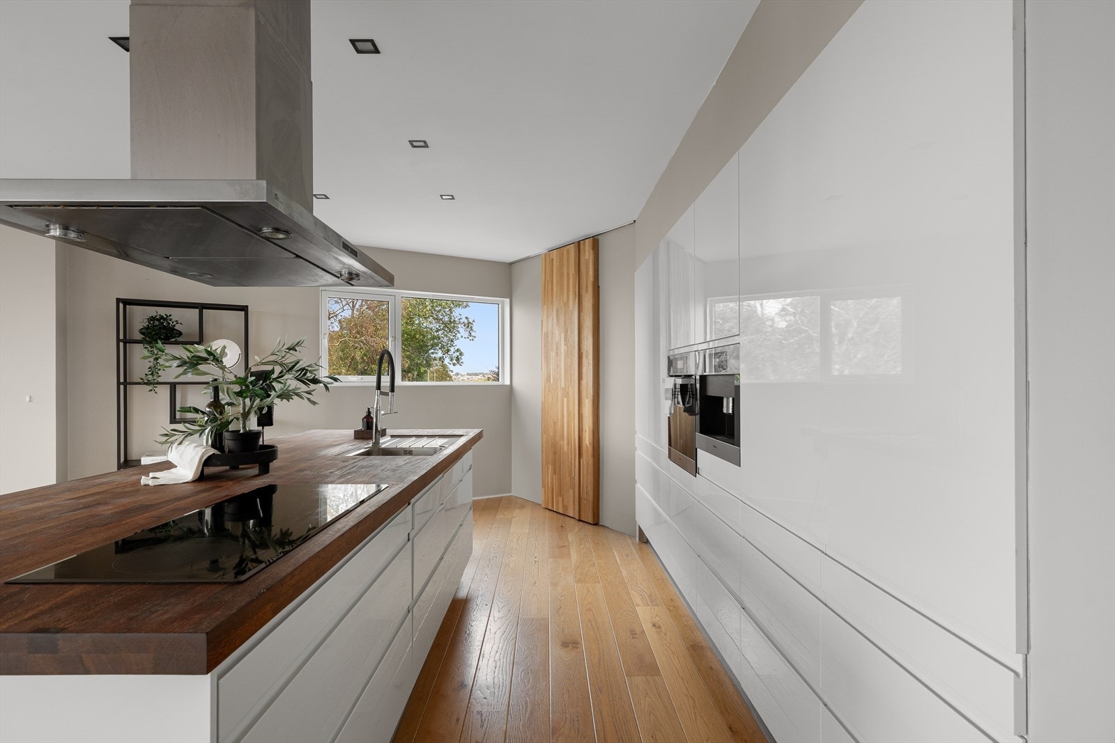 Gjennomført kjøkken med integrert kaffemaskin, hvite fronter og store vindusflater som gir naturlig lys. Galleribilde