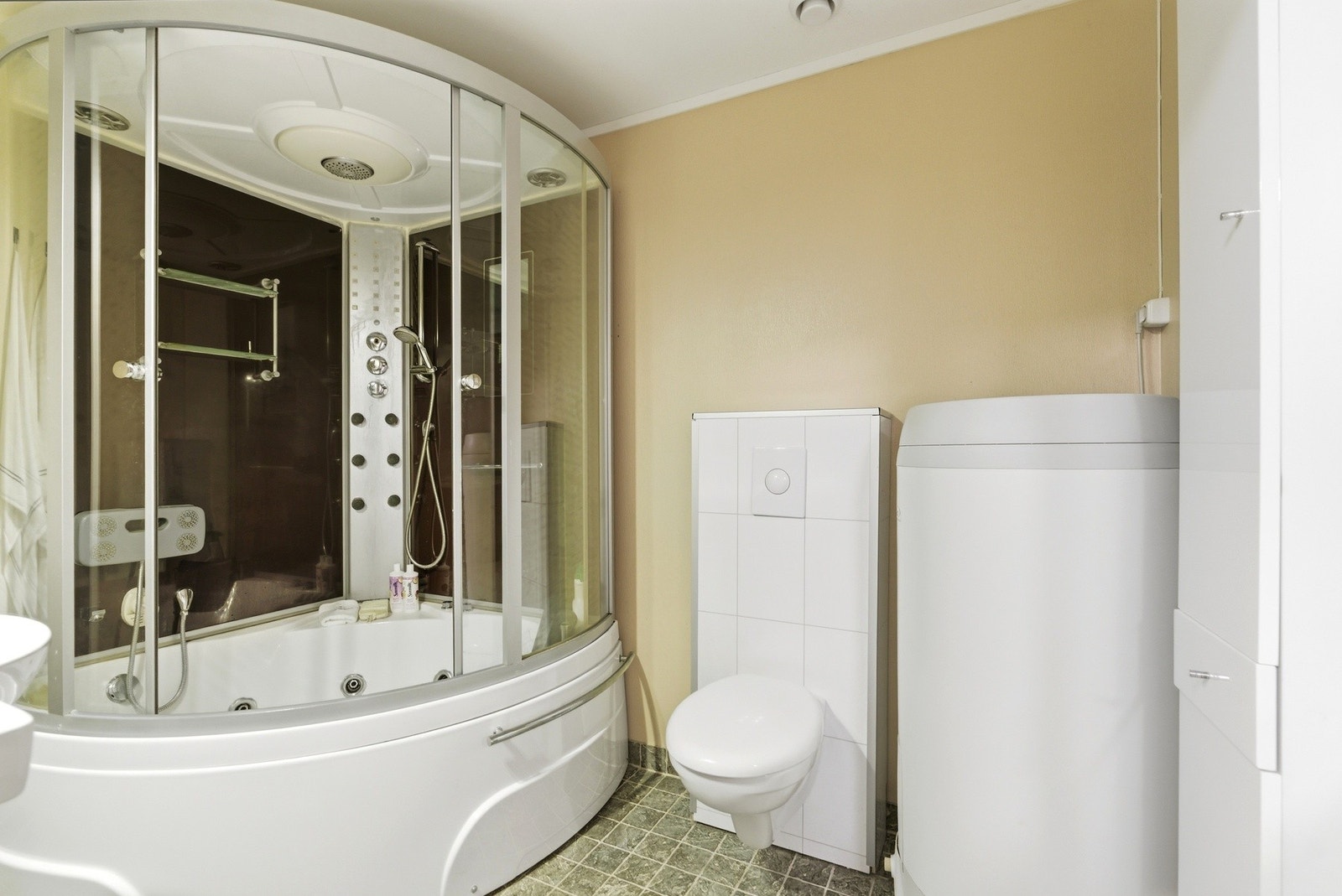 Badet har innredning med nedfelt servant, veggmontert toalett og dusjkabinett med badekar. Galleribilde