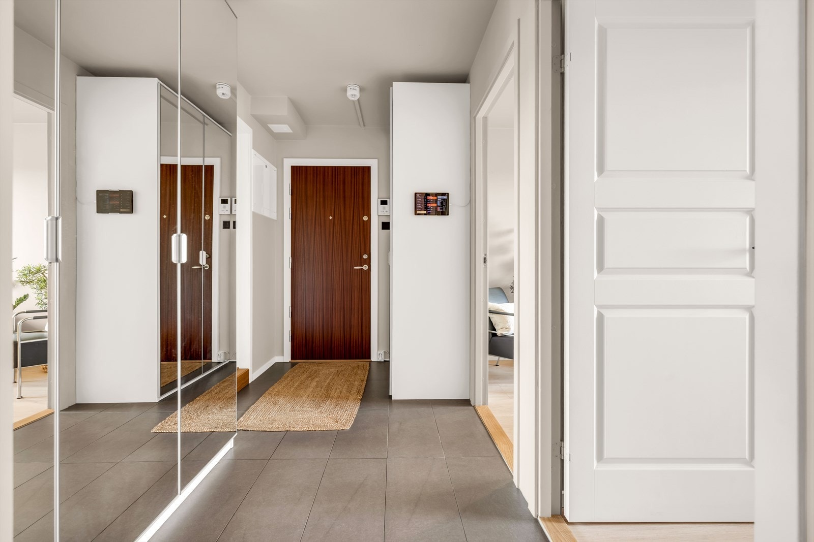 Velkommen inn! Entréen gir et ryddig og innbydende førsteinntrykk. Gulvet er flislagt med varmekabler som gir ekstra komfort, og garderobeskap med speilfronter gir god plass til yttertøy og sko. Galleribilde