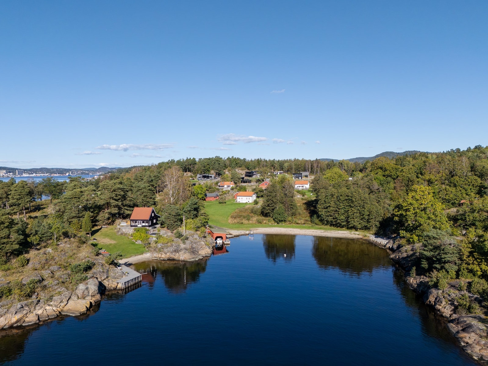 En idyllisk vik med sandstrand og båthus i nærområdet. Galleribilde