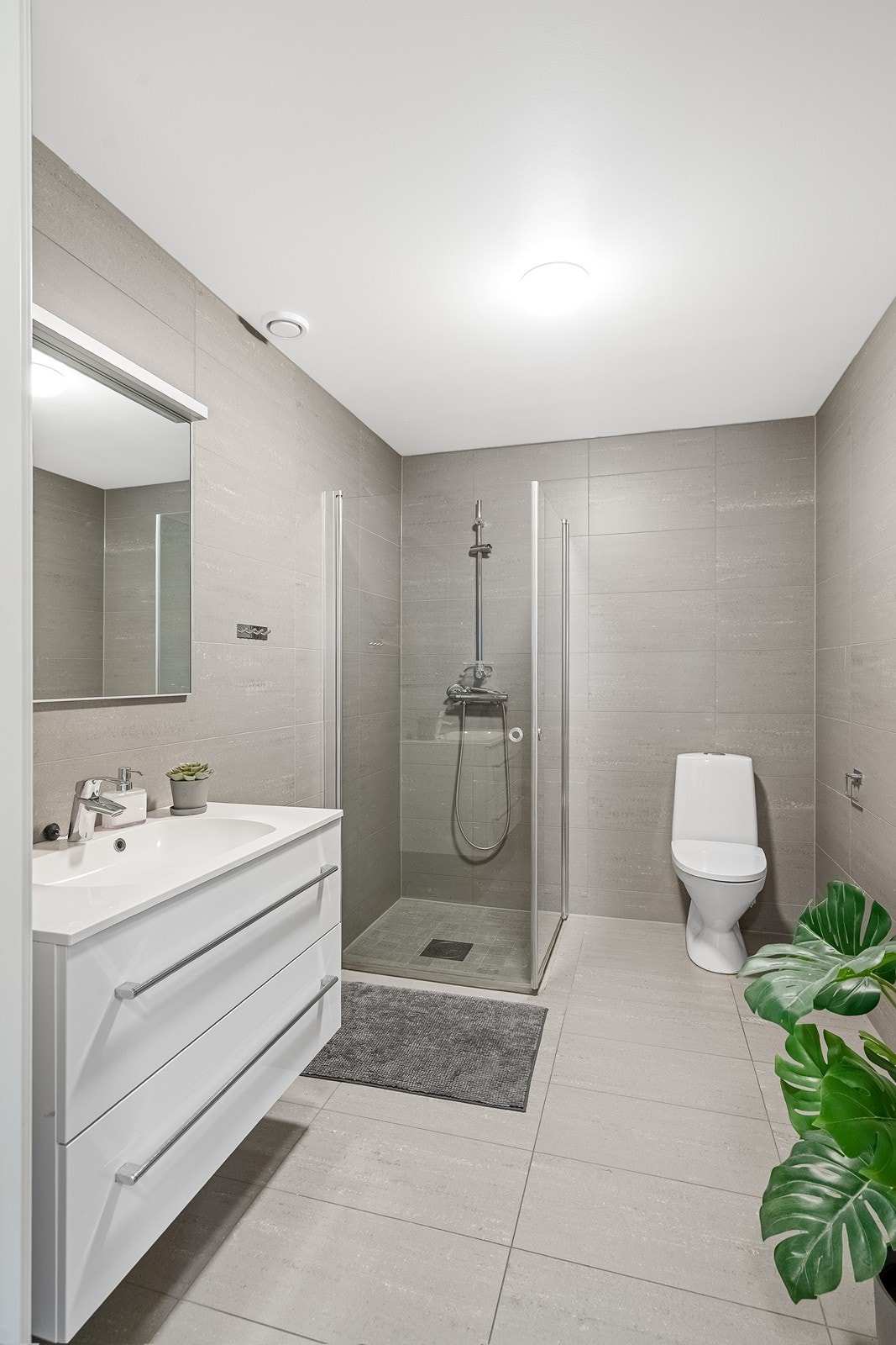 Elegant bad med store fliser i lune toner. Dusjhjørne, moderne innredning og god oppbevaring. Galleribilde