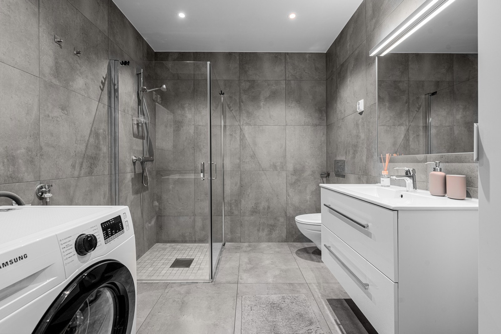 Badet er innredet med vegghengt toalett, helservant på skuffeseksjon, dusjhjørne og opplegg for vaskemaskin. Galleribilde