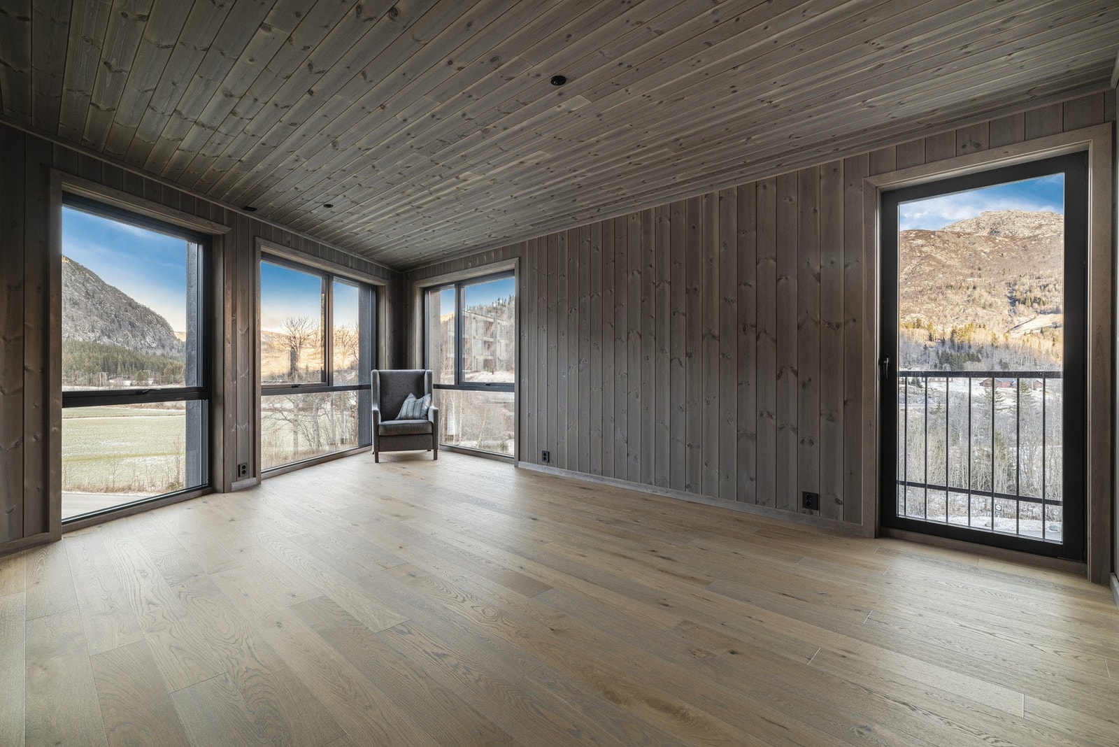 Stor stue med store vinduer og flott utsikt. Vegger i stående beiset interiørpanel i furu, gulv i 1-stavs eikeparkett Galleribilde