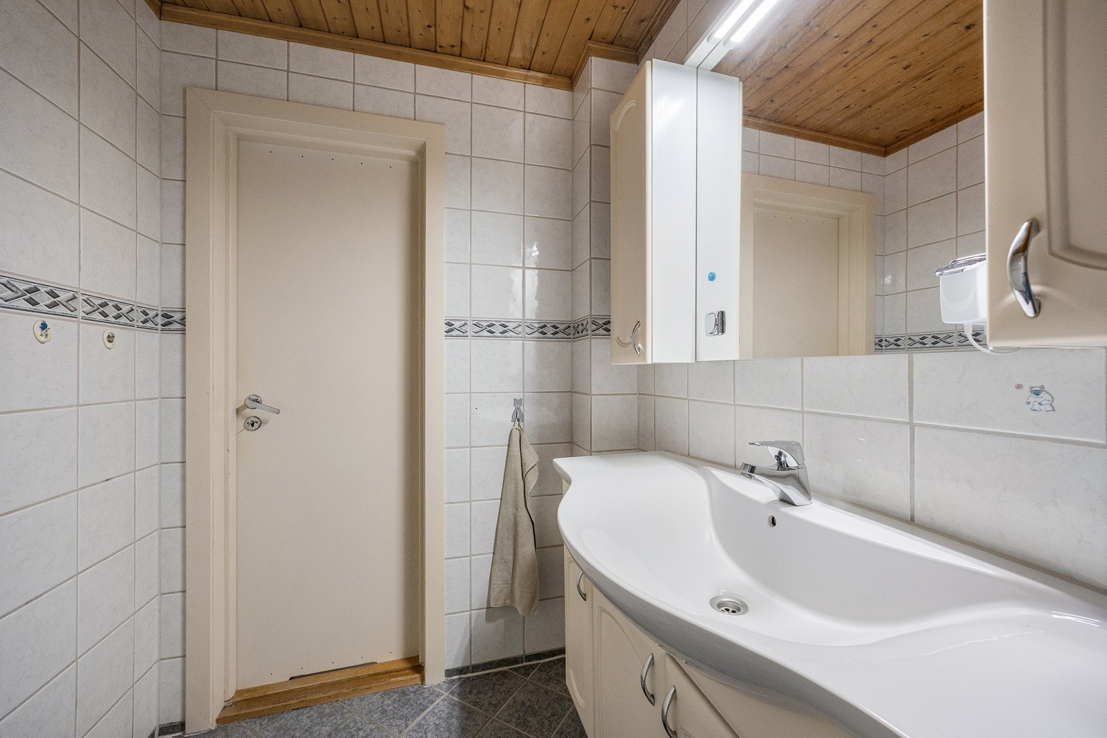 Badet innredet med vegg- og gulvfliser i ulike grånyanser. Boden på hovedplanet er utstyrt med opplegg for vaskemaskin. Galleribilde