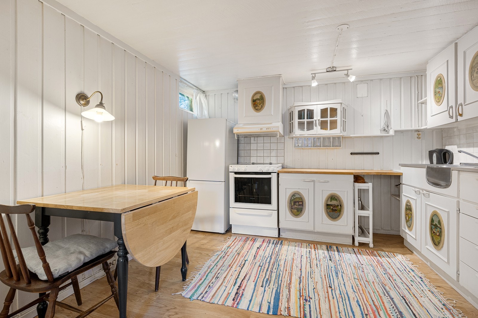 Kjøkkeninnredningen i underetasjen har hvite, profilerte fronter, vitrineskap, heltre benkeplate og dobbel oppvaskkum av stål. Galleribilde