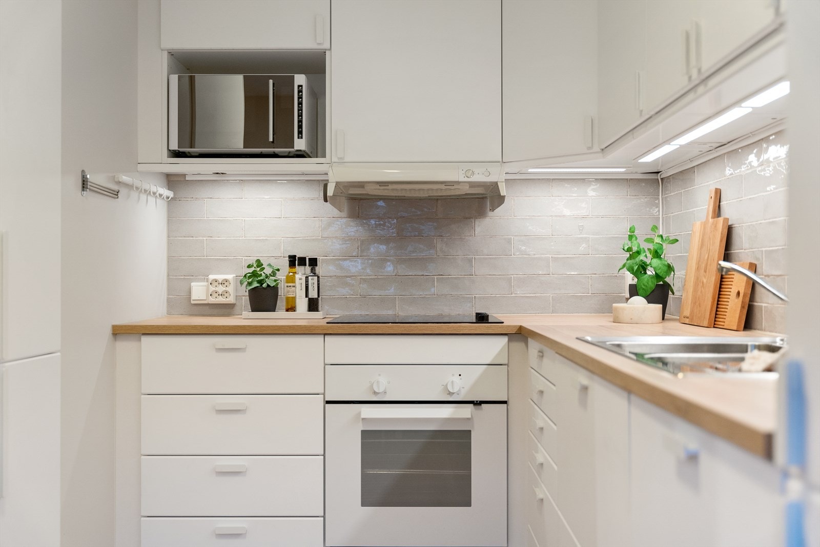 Kjøkkeninnredning med glatte fronter og rikelig med skap- og benkeplass. Her er det fliser på vegg over benkeplate av laminat med nedfelt kum i rustfritt stål. Galleribilde