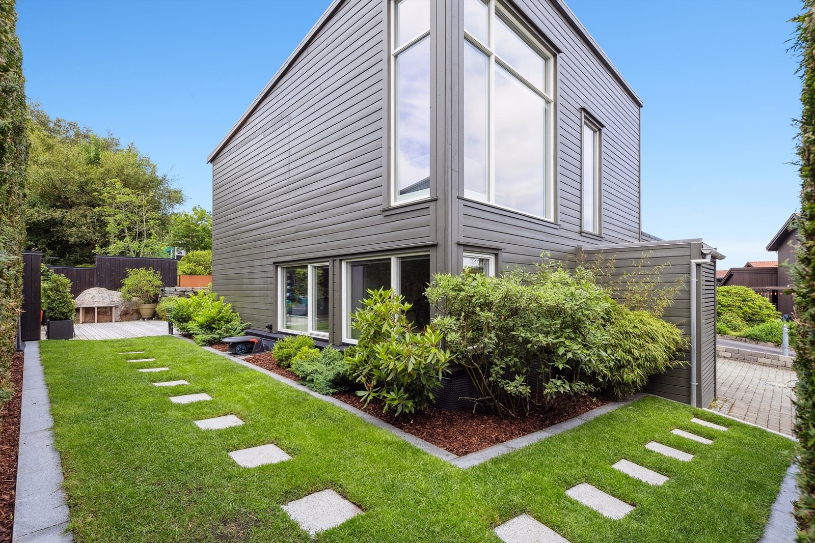 Tomten er pent opparbeidet med steinbelagt gårdsplass, vintergrønn hekk som skjermer hagen, og vakre detaljer som bed og heller fra gårdsplass til terrasse. Galleribilde