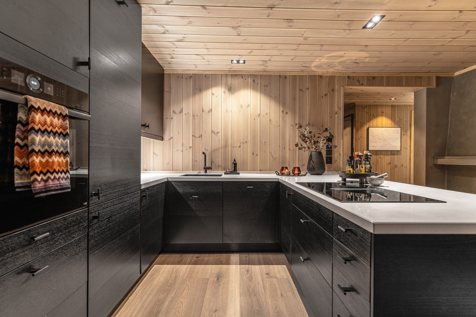 Lekkert og stilrent kjøkken med svarte fronter og lyse trepaneler på veggen som skaper lun og fin harmoni. Galleribilde