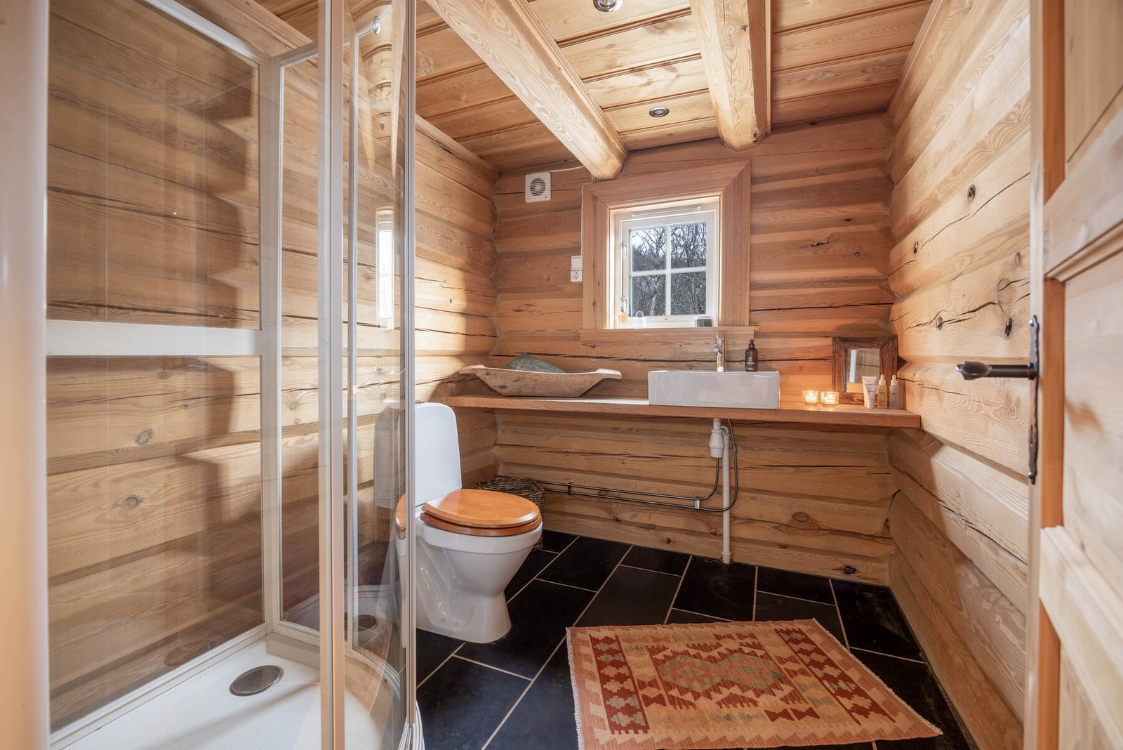 Et stemningsfullt bad der fliser møter tømmer - en harmonisk kombinasjon av komfort og hyttekos. Galleribilde