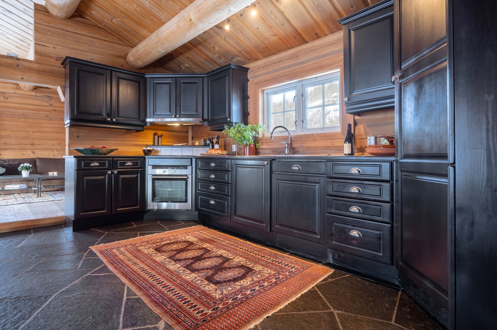 Et tidsriktig kjøkken i mørke toner, der flisbelagt benkeplate og integrerte hvitevarer smelter sømløst inn i tømmerets varme. Galleribilde